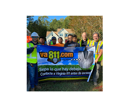 Eight excavation safety training participants display Spanish language banner at an outdoor residential excavation site.